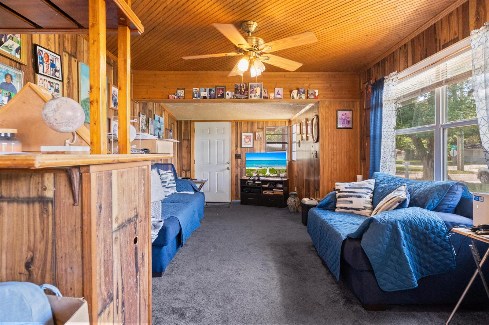 A living room with wood-paneled walls, a ceiling fan, blue sofas, and a television — 1804 S 30th S, Fort Pierce FL 34947, FORT PIERCE, FL