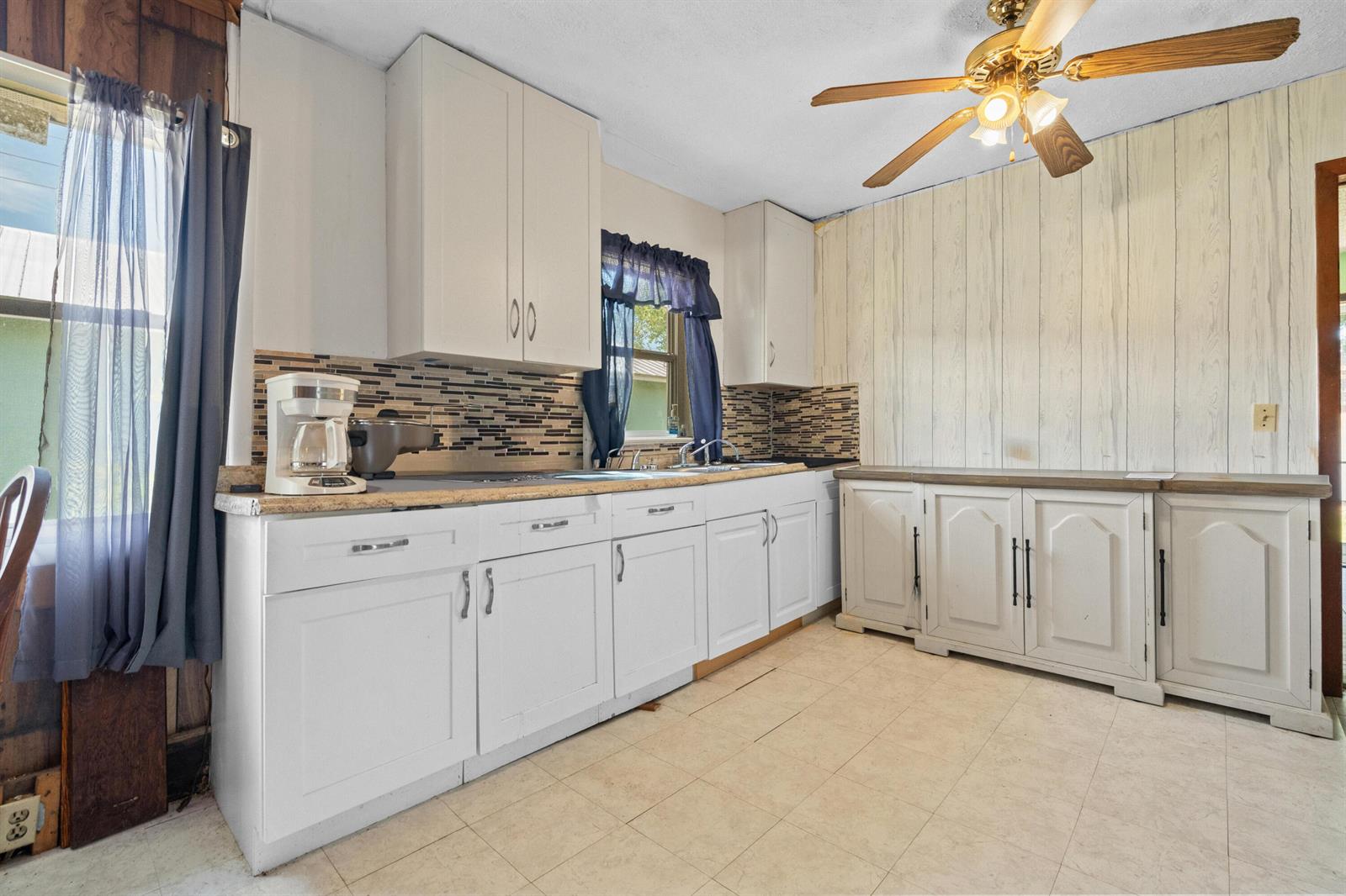 A kitchen features white cabinets, a tiled backsplash, wood-paneled walls, and a ceiling fan — 1804 S 30th S, Fort Pierce FL 34947, FORT PIERCE, FL