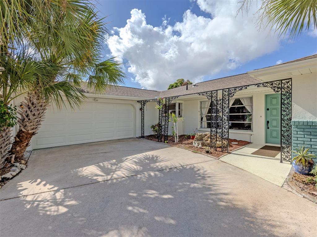 A single-story house with a white garage, decorative iron porch supports, and a teal door — 1480 LAKESIDE DRIVE, VENICE, FL