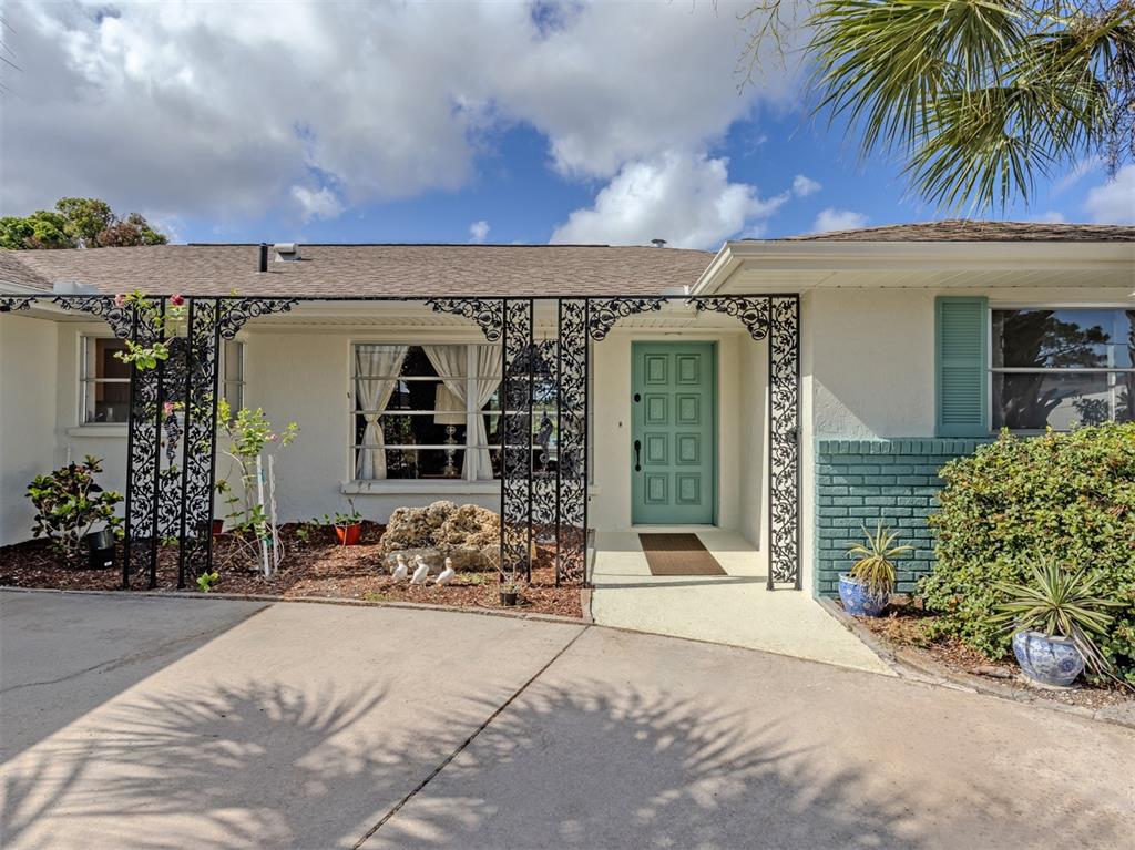A single-story house exterior features a teal front door, decorative iron supports, and brick accents — 1480 LAKESIDE DRIVE, VENICE, FL
