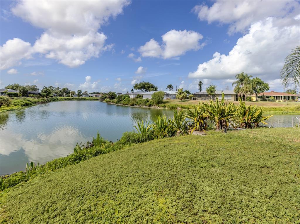 A grassy slope leads down to a pond with houses visible in the background — 1480 LAKESIDE DRIVE, VENICE, FL