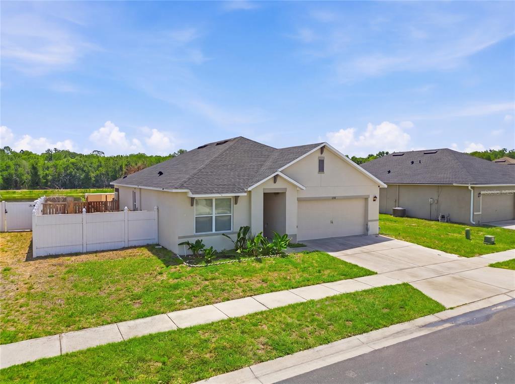 A single-story suburban house with a tan stucco exterior, a two-car garage, and white fencing — 6194 GREY HERON DRIVE, WINTER HAVEN, FL