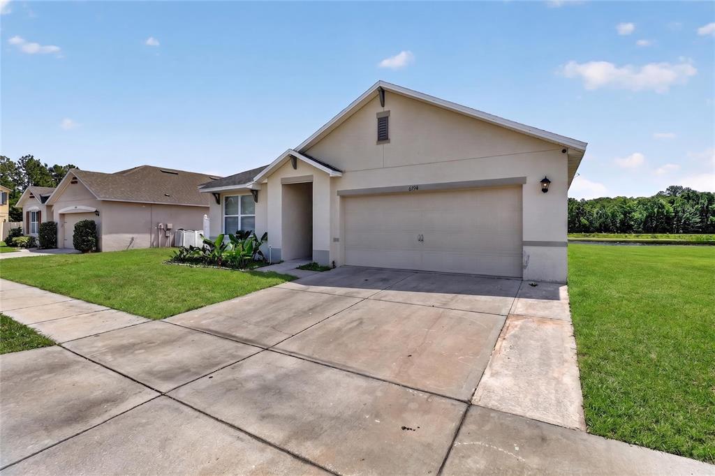 A single-story house with a two-car garage, a concrete driveway, and a grassy lawn — 6194 GREY HERON DRIVE, WINTER HAVEN, FL