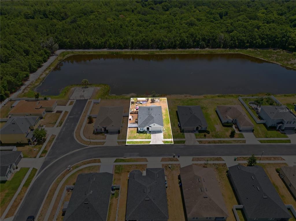An aerial view shows a single-family home with a fenced backyard bordering a pond — 6194 GREY HERON DRIVE, WINTER HAVEN, FL