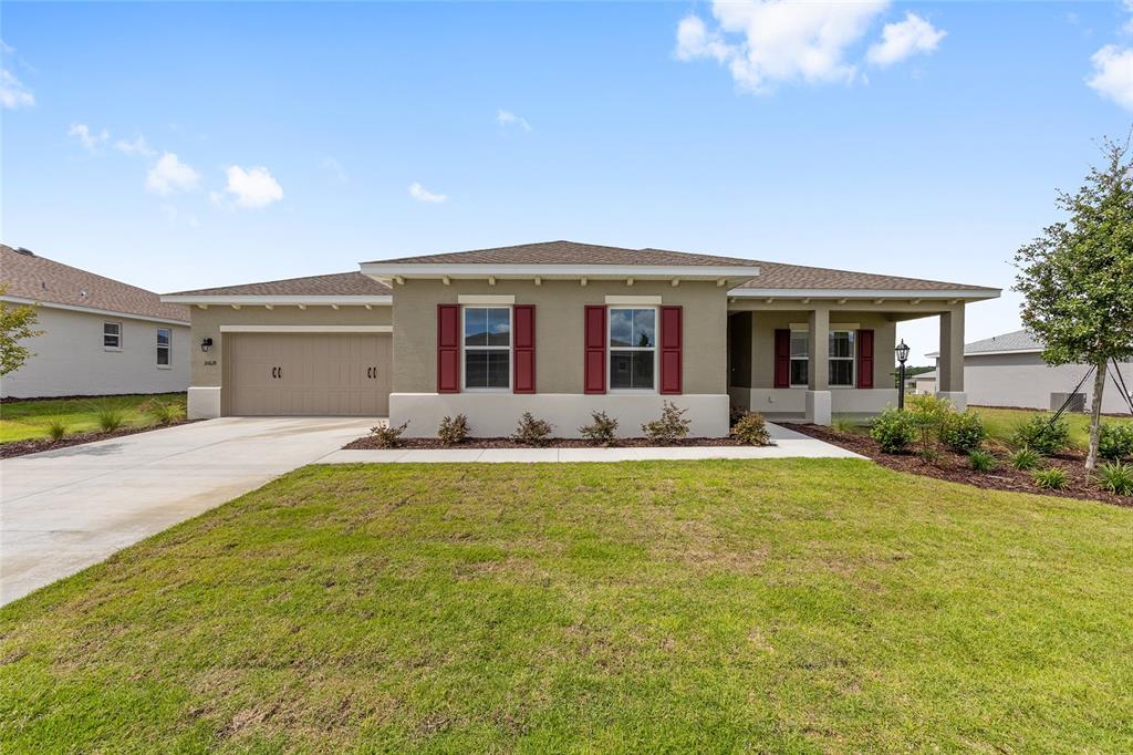 A single-story house features a tan exterior, red shutters, a two-car garage, and a lawn — 10618 SW 101ST LANE ROAD, OCALA, FL