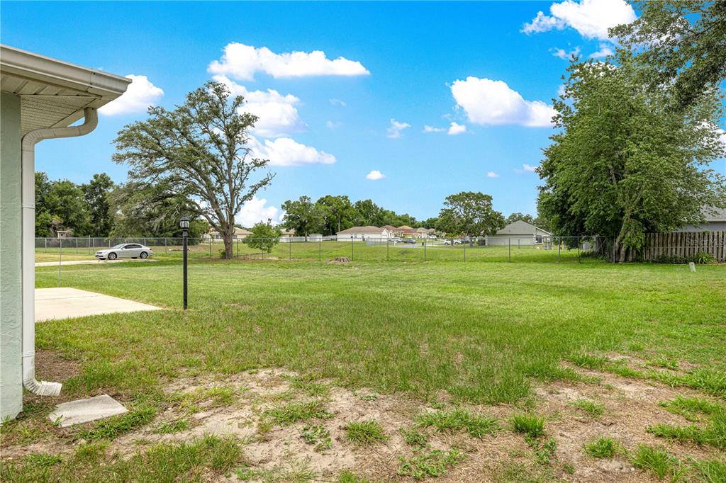 A view of a large, grassy backyard with a chain-link fence and surrounding trees — 6185 SW 84TH STREET, OCALA, FL