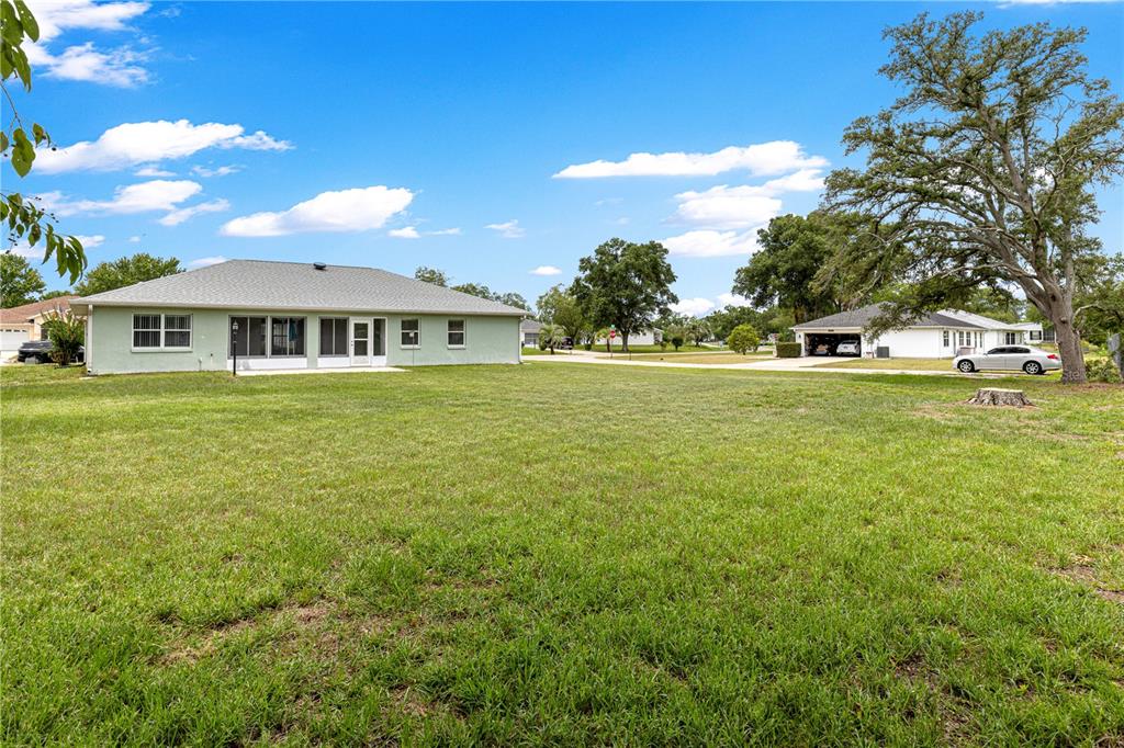 A wide, grassy backyard view of a light green single-story house with a hip roof — 6185 SW 84TH STREET, OCALA, FL