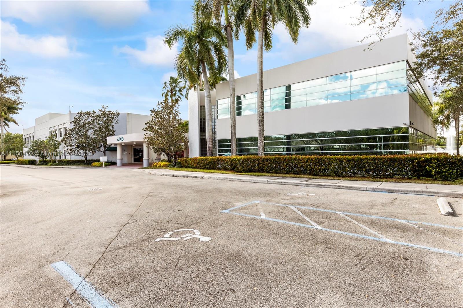 A modern two-story office building with a parking lot and palm trees in the foreground — 1455 N Park Dr, Weston FL 33326, WESTON, FL
