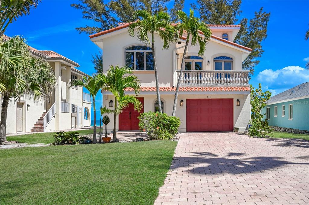 A two-story house with a red garage door, a balcony, and palm trees in front — 889 N SHORE DRIVE, ANNA MARIA, FL