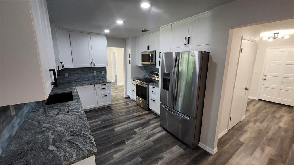 A kitchen features white cabinets, granite countertops, stainless steel appliances, and wood-look flooring — 8531 PORT SAID STREET, ORLANDO, FL
