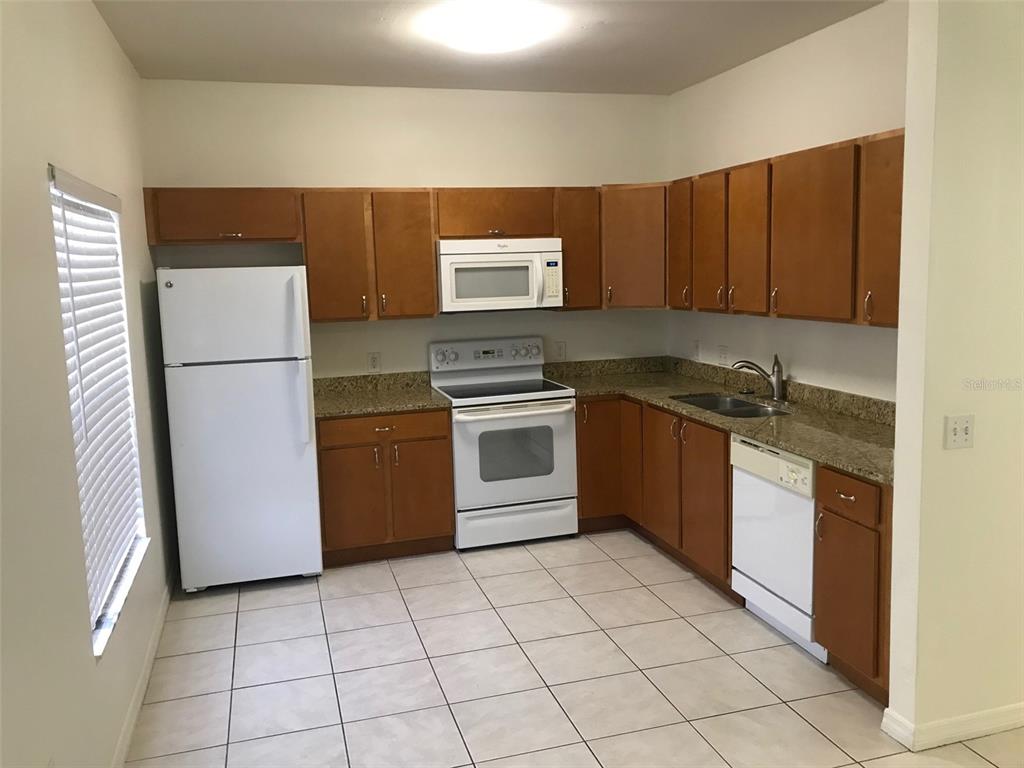 A kitchen features wood cabinets, granite countertops, white appliances, and light-colored tile flooring — 7635 PLANTATION CIRCLE UNIT 7635, BRADENTON, FL