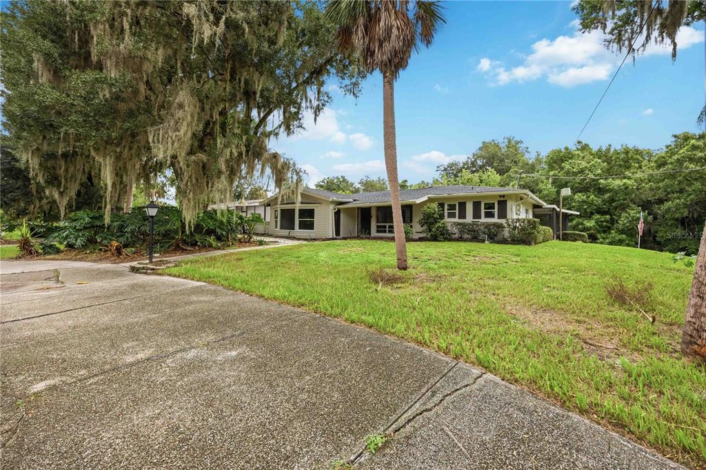A single-story house with a light-colored exterior sits on a grassy lot with large trees — 5430 TIMBERLANE ROAD, LAKE WALES, FL