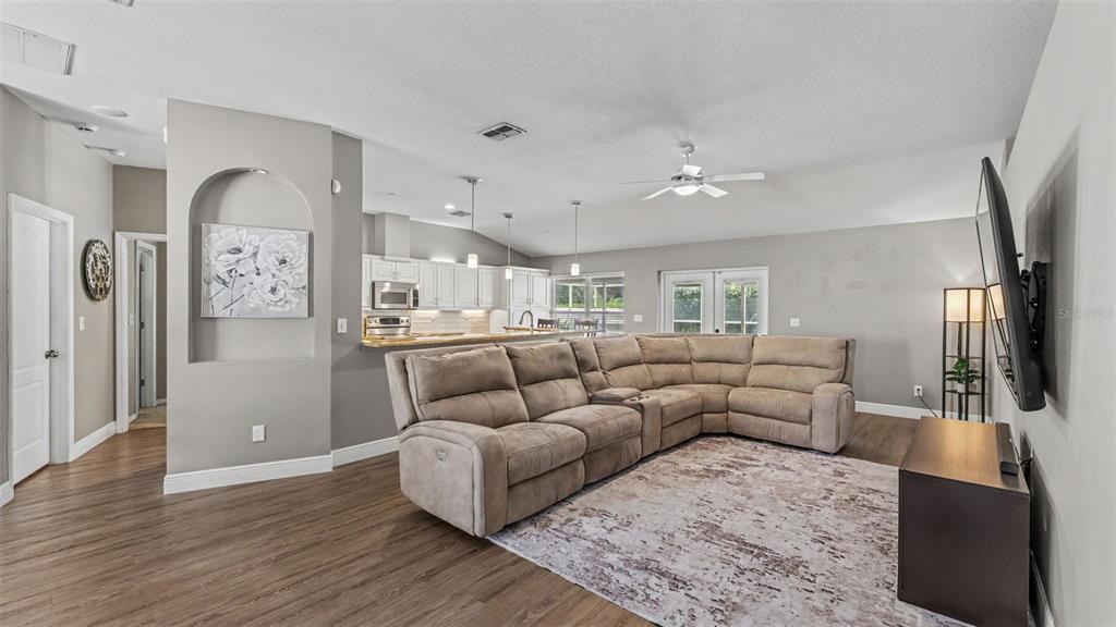 A living room with a large sectional sofa, wood-look flooring, and an open-concept kitchen — 2219 TOWERING OAKS CIRCLE, SEFFNER, FL