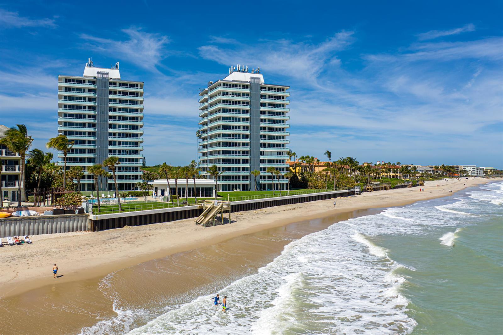 Two high-rise residential buildings stand along a sandy beach with ocean waves and palm trees — 3554 Ocean Drive, Vero Beach FL 32963, VERO BEACH, FL