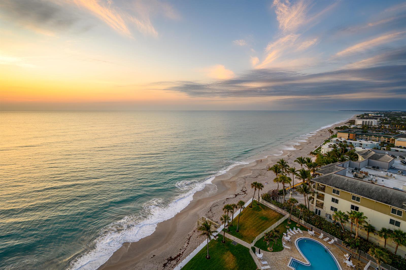 An aerial view of a beachfront resort with a swimming pool and palm trees at sunset — 3554 Ocean Drive, Vero Beach FL 32963, VERO BEACH, FL