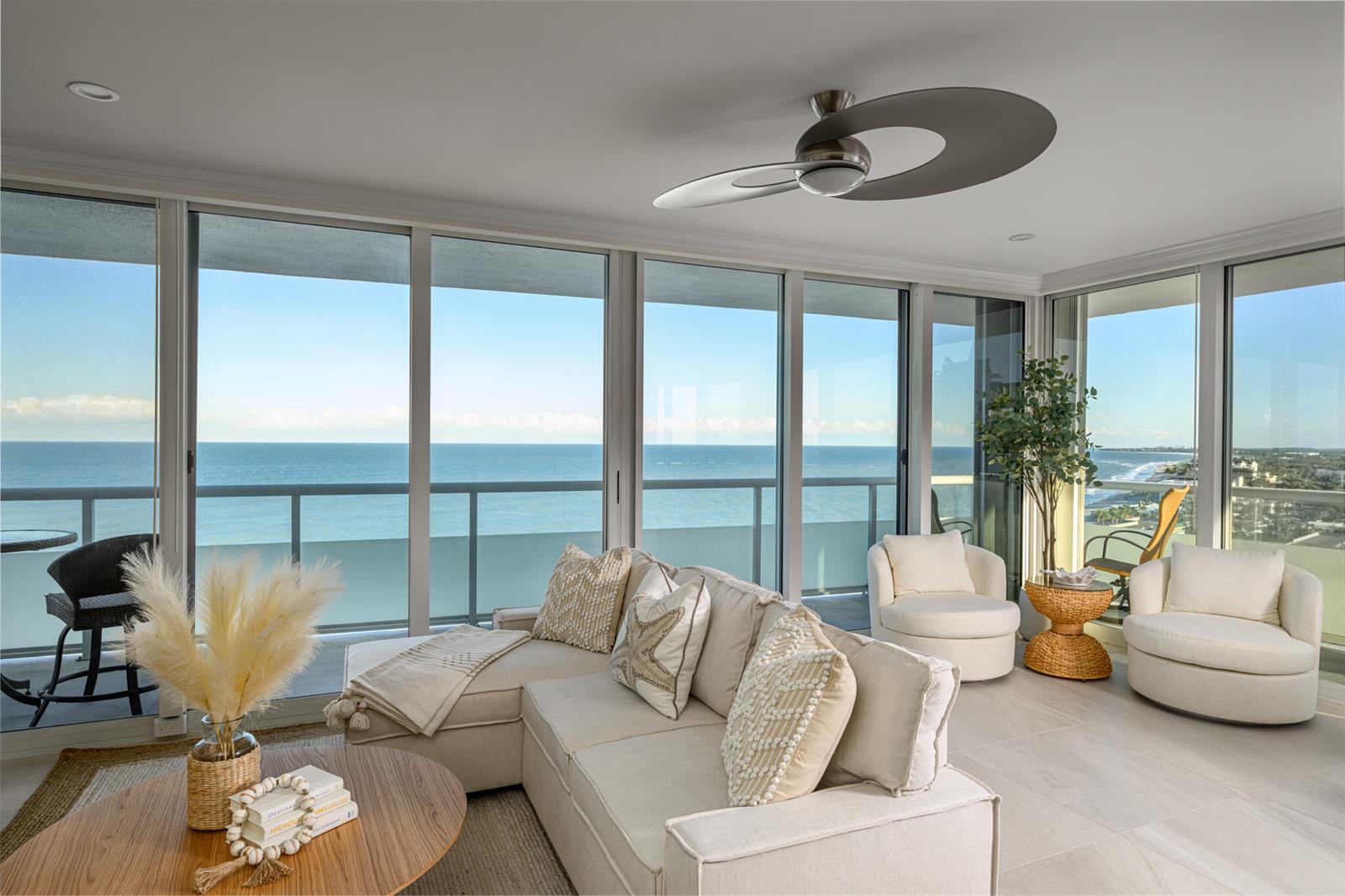 A bright living room features a sectional sofa, two swivel chairs, and floor-to-ceiling ocean views — 3554 Ocean Drive, Vero Beach FL 32963, VERO BEACH, FL