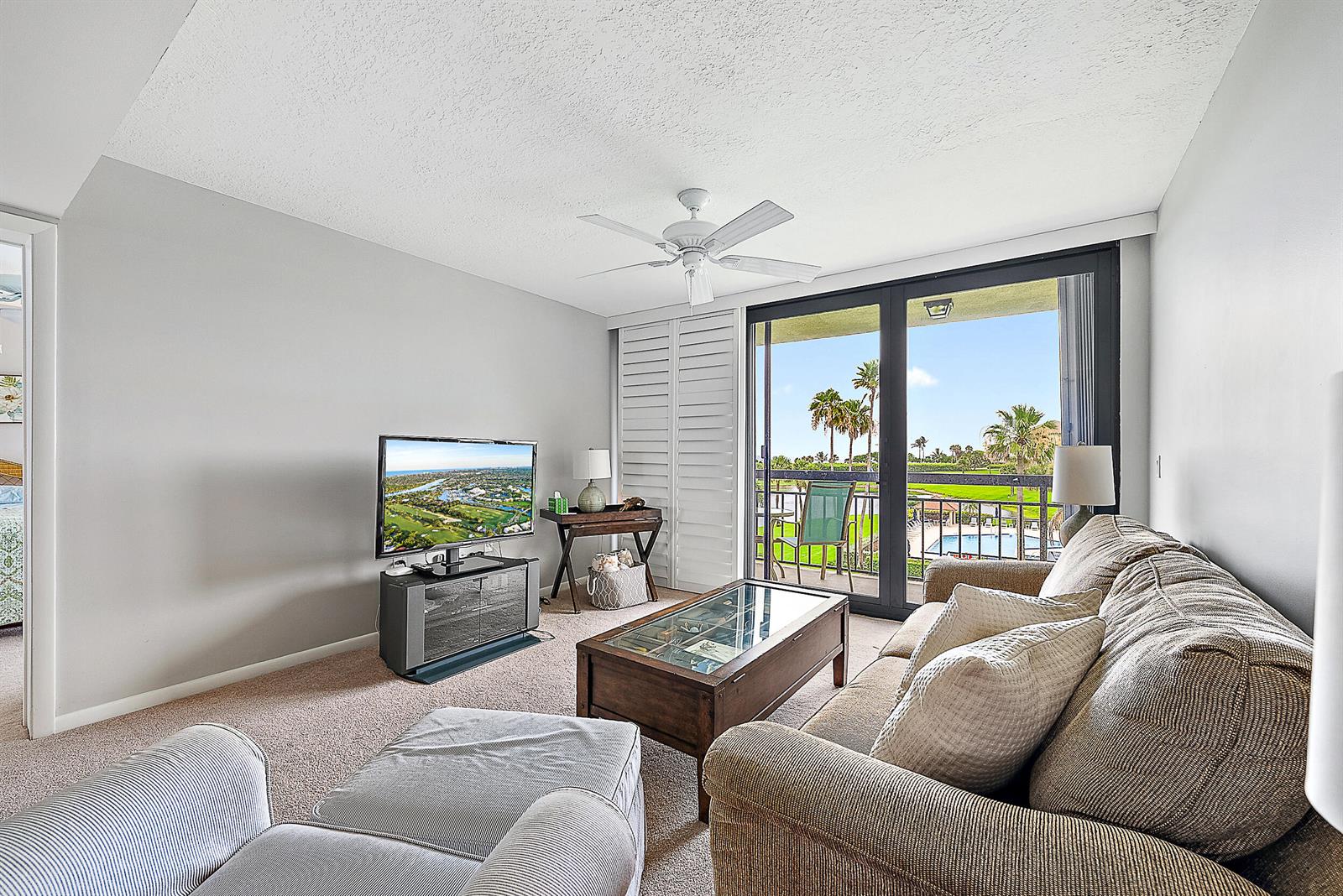 A living room features a sofa, television, coffee table, and sliding doors opening to a balcony — 301 S Seas Drive # 305, Jupiter FL 33477, JUPITER, FL
