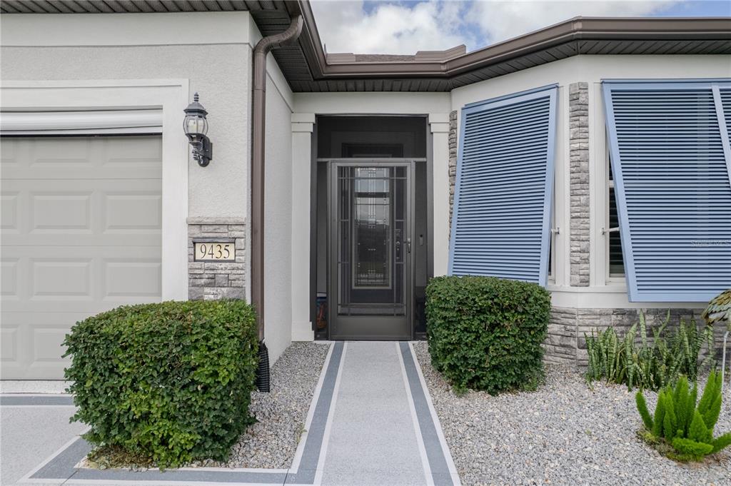 The exterior of a house features a front door, two bushes, and blue window shutters — 9435 SW 52ND LOOP, OCALA, FL