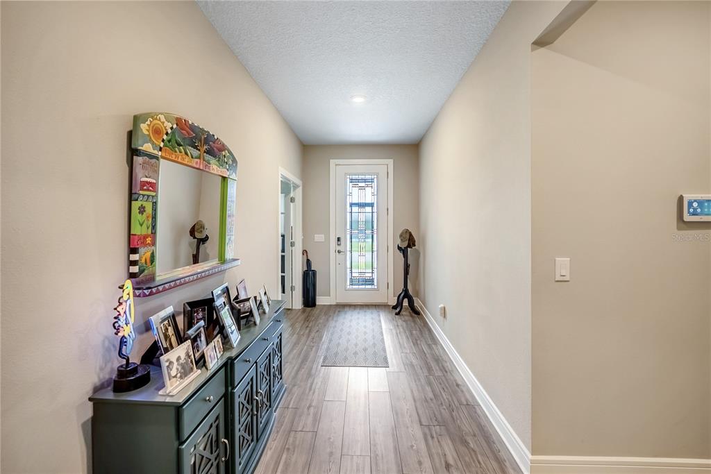 A hallway with wood-look flooring, a console table, a decorative mirror, and a glass-paneled front door — 9435 SW 52ND LOOP, OCALA, FL