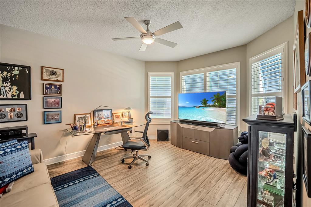 A home office features a glass desk, a television on a console, and wood-look flooring — 9435 SW 52ND LOOP, OCALA, FL