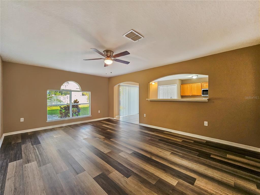 A living room with wood-look flooring, a ceiling fan, and a pass-through to the kitchen — 3650 FYFIELD COURT, LAND O LAKES, FL
