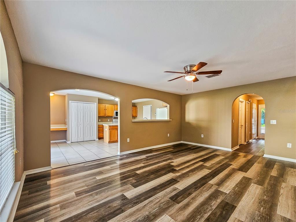 A living room with wood-look flooring, a ceiling fan, and arched openings to the kitchen — 3650 FYFIELD COURT, LAND O LAKES, FL