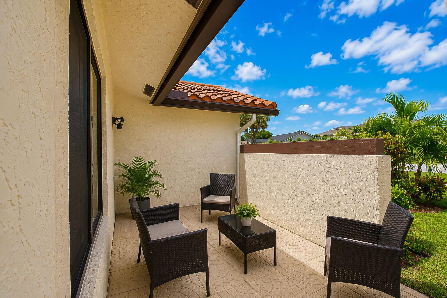 A patio with wicker furniture, a small table, and a privacy wall under a blue sky — 22209 Morning Glory Terrace, Boca Raton FL 33433, BOCA RATON, FL
