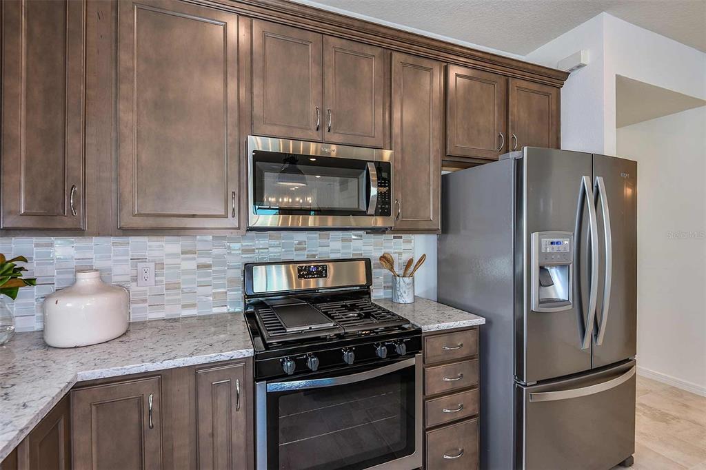 A kitchen features dark wood cabinets, stainless steel appliances, and a light-colored granite countertop — 2621 HAMMOCK HARBOR AVENUE, ST CLOUD, FL