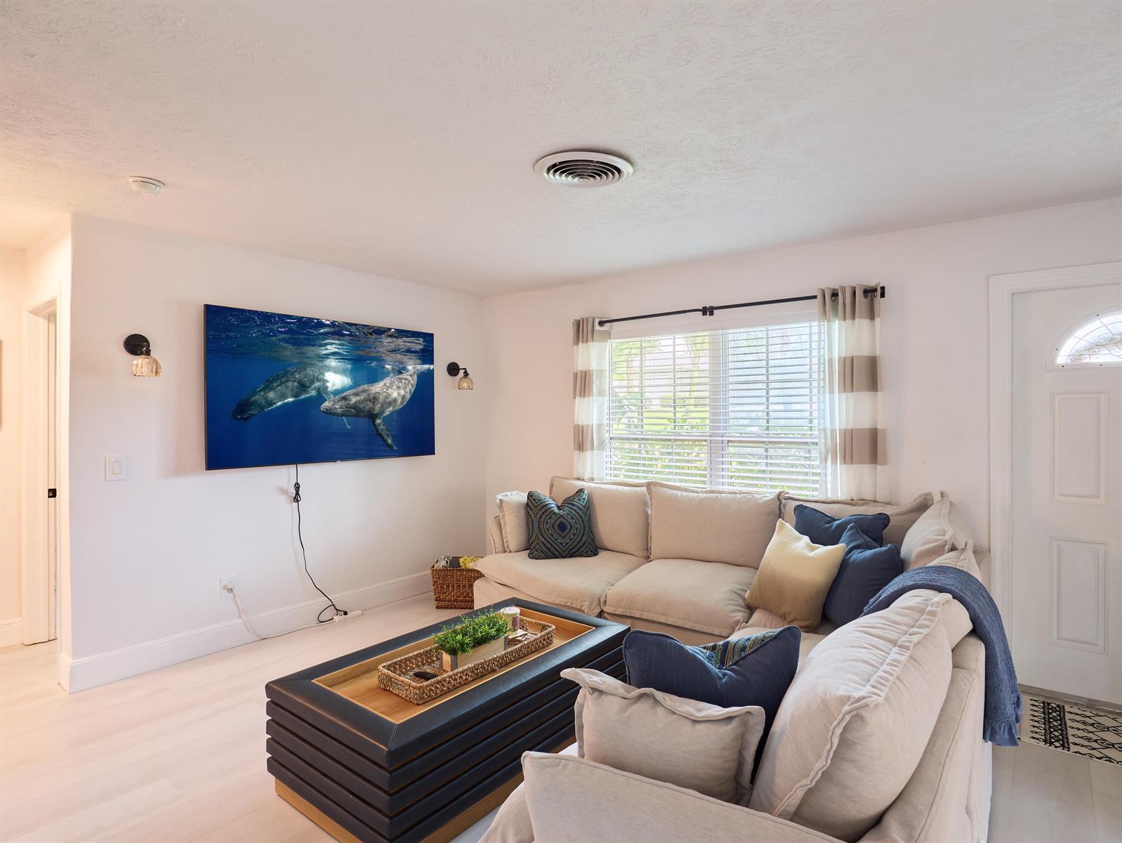 A living room features a wall-mounted television, a large sectional sofa, and a coffee table — 3743 NE Barbara Drive, Jensen Beach FL 34957, JENSEN BEACH, FL