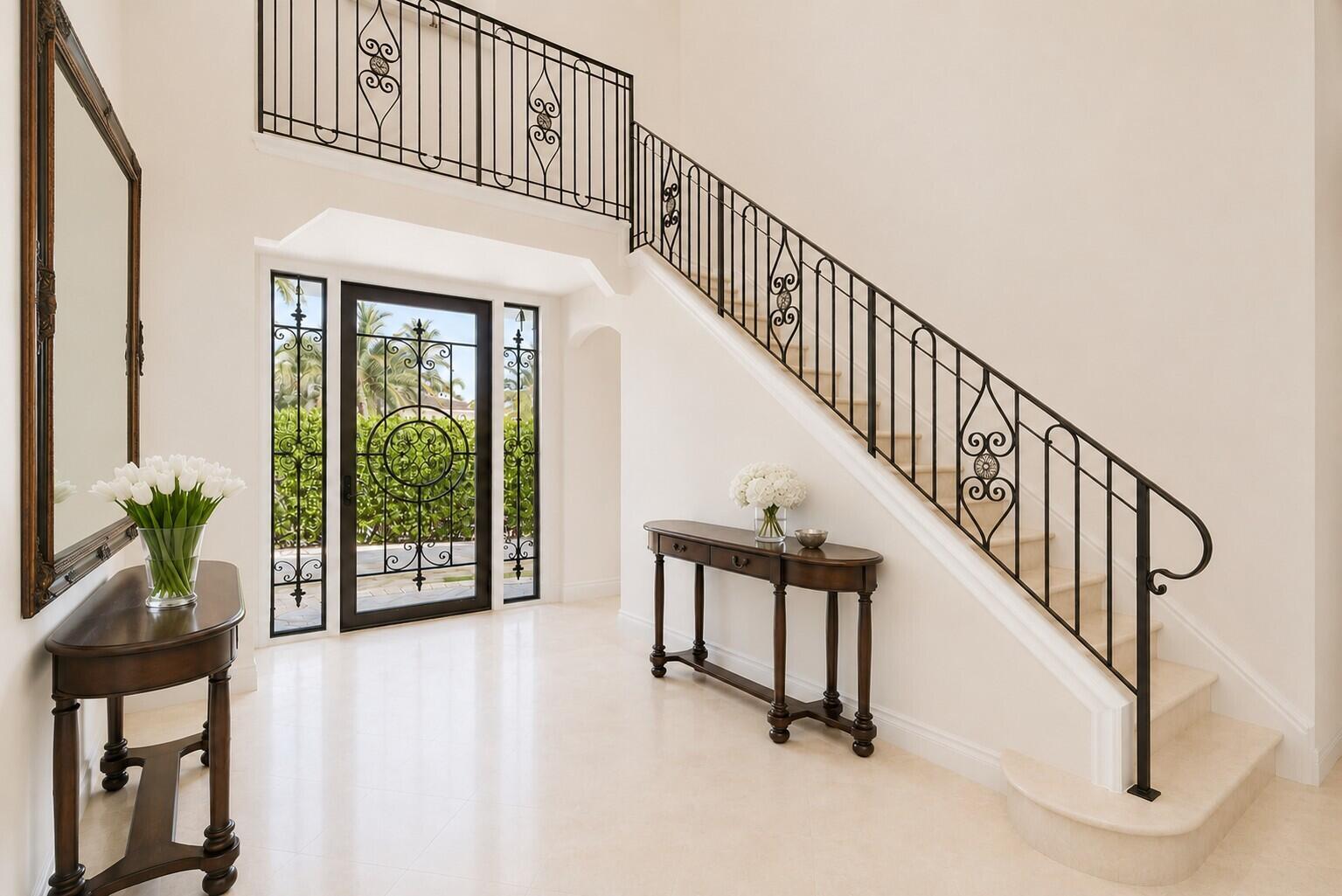 A bright foyer features a grand staircase with ornate iron railings and two wooden tables — 286 Jamaica Lane, Palm Beach FL 33480, PALM BEACH, FL