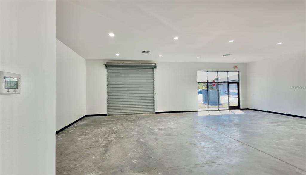 An empty commercial space features a concrete floor, white walls, recessed lighting, and a roll-up door — 727 TILLMAN PLACE UNIT 101, PLANT CITY, FL