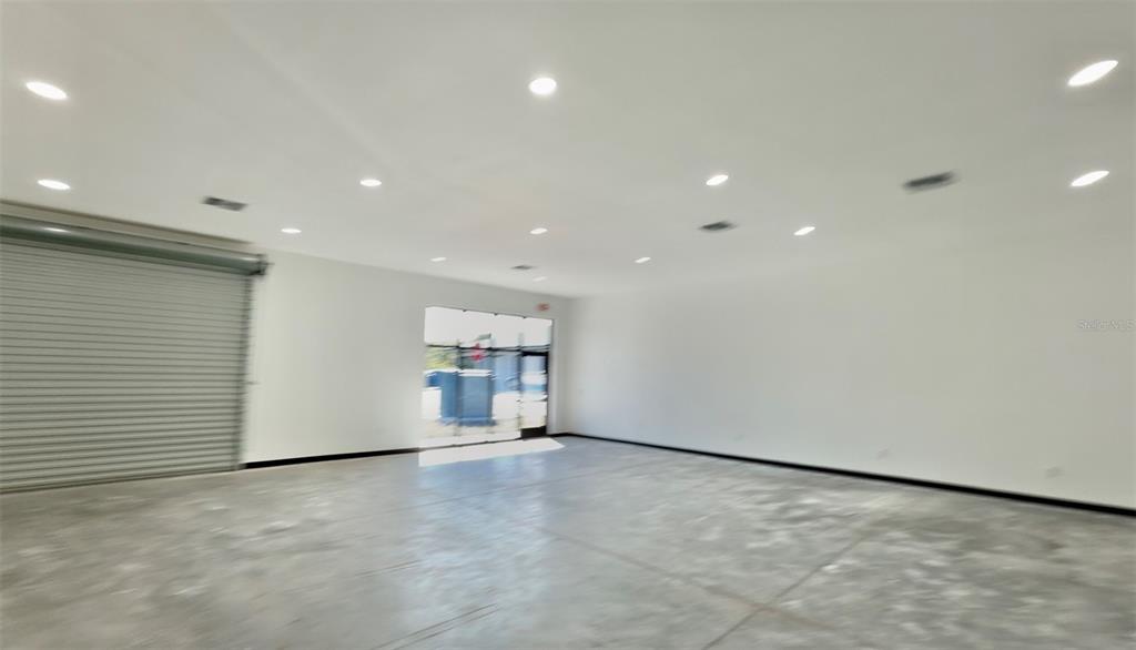 An empty commercial space features a roll-up door, concrete floors, and recessed ceiling lighting — 727 TILLMAN PLACE UNIT 101, PLANT CITY, FL