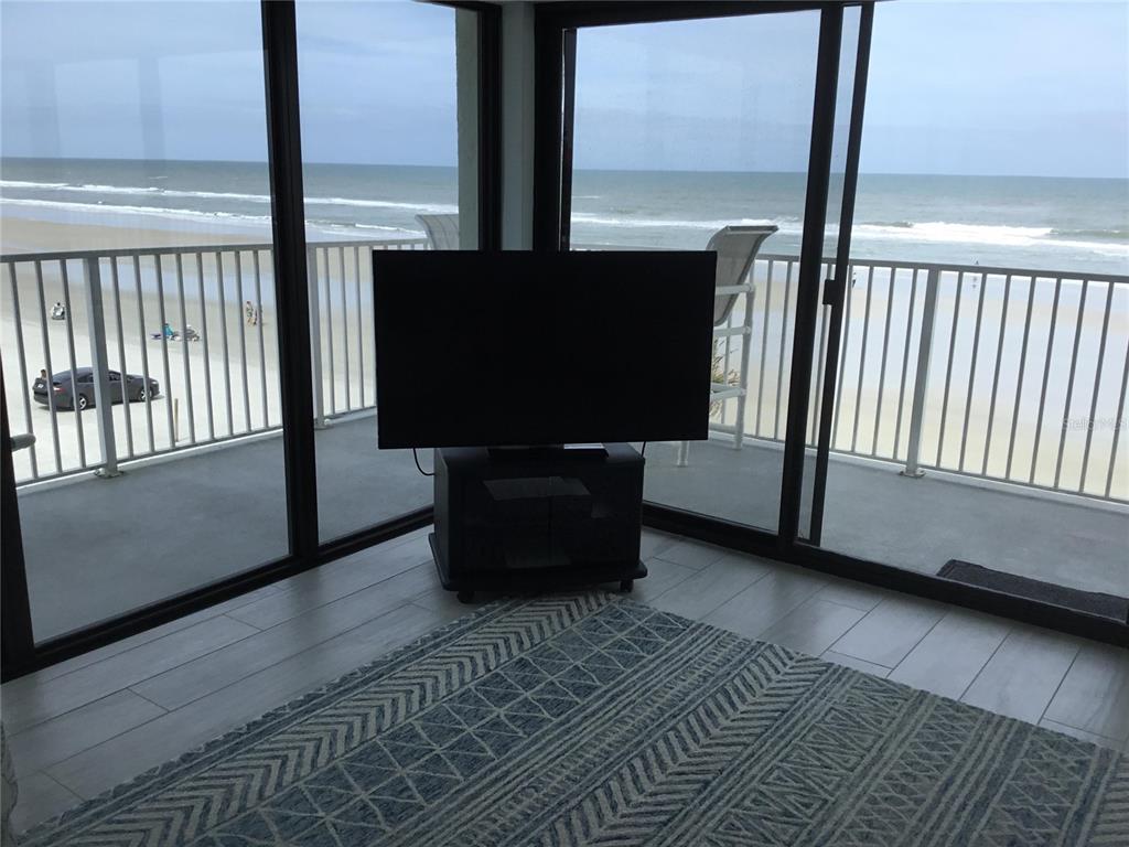 A television on a stand sits in front of floor-to-ceiling windows overlooking the beach — 1571 S ATLANTIC AVENUE UNIT 310, NEW SMYRNA BEACH, FL