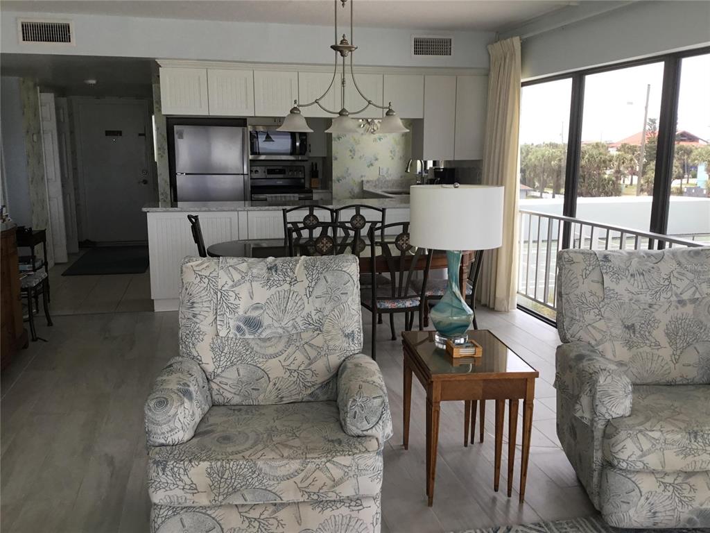 A living area with patterned armchairs and a dining set faces a kitchen and balcony — 1571 S ATLANTIC AVENUE UNIT 310, NEW SMYRNA BEACH, FL