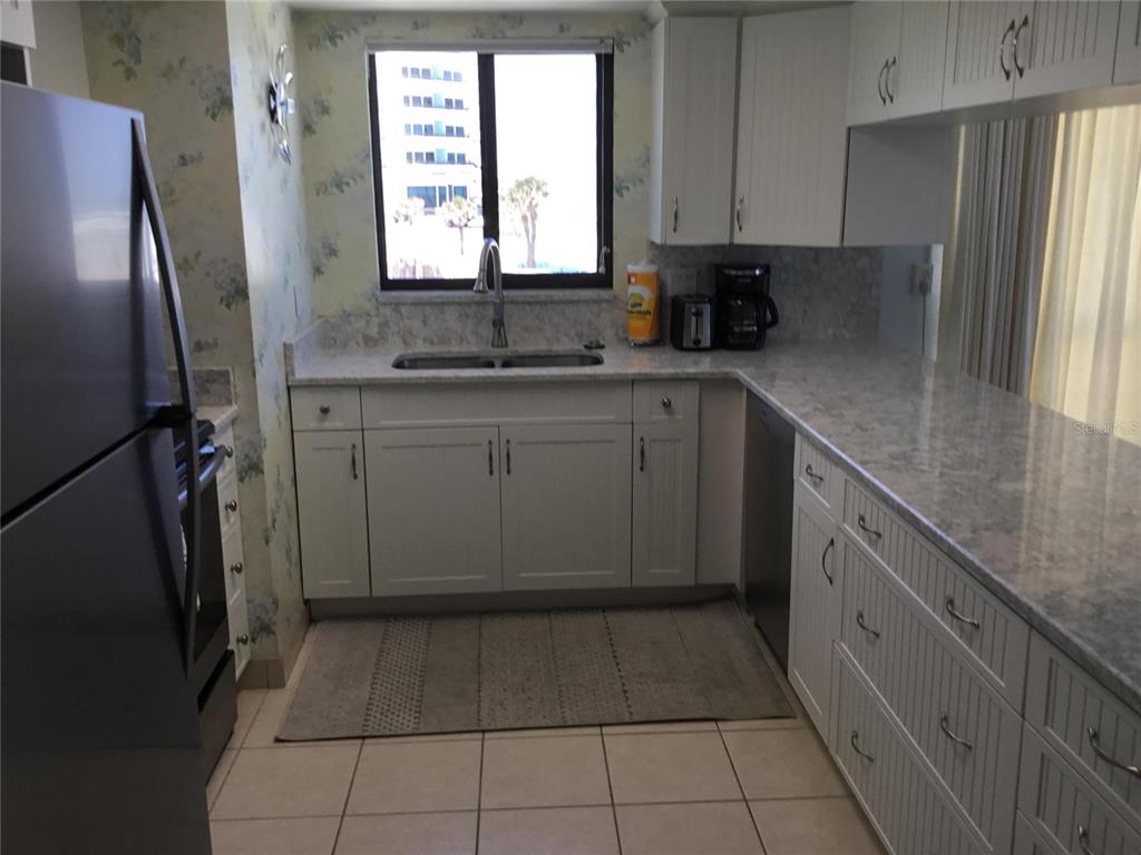 A kitchen features white cabinets, granite countertops, a stainless steel refrigerator, and floral wallpaper — 1571 S ATLANTIC AVENUE UNIT 310, NEW SMYRNA BEACH, FL
