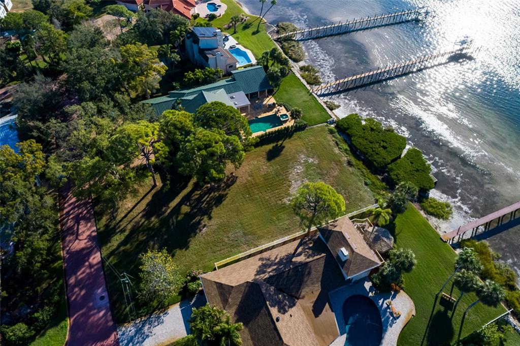 An aerial view shows two waterfront houses with swimming pools, docks, and large grassy yards — FRIENDLY WAY S, ST PETERSBURG, FL