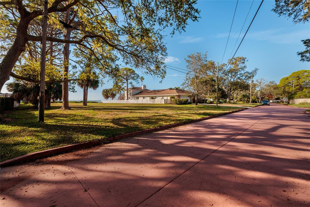 A residential street with a reddish-tinted road leads toward a house behind a white fence — FRIENDLY WAY S, ST PETERSBURG, FL