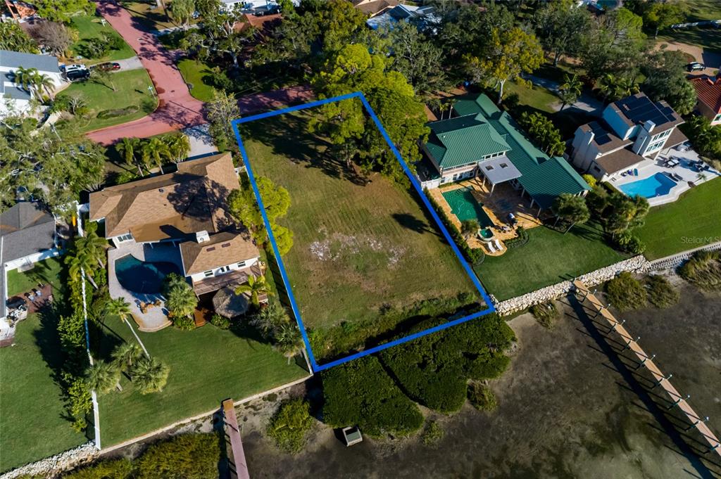 An aerial view shows a vacant waterfront lot outlined in blue between two residential properties — FRIENDLY WAY S, ST PETERSBURG, FL