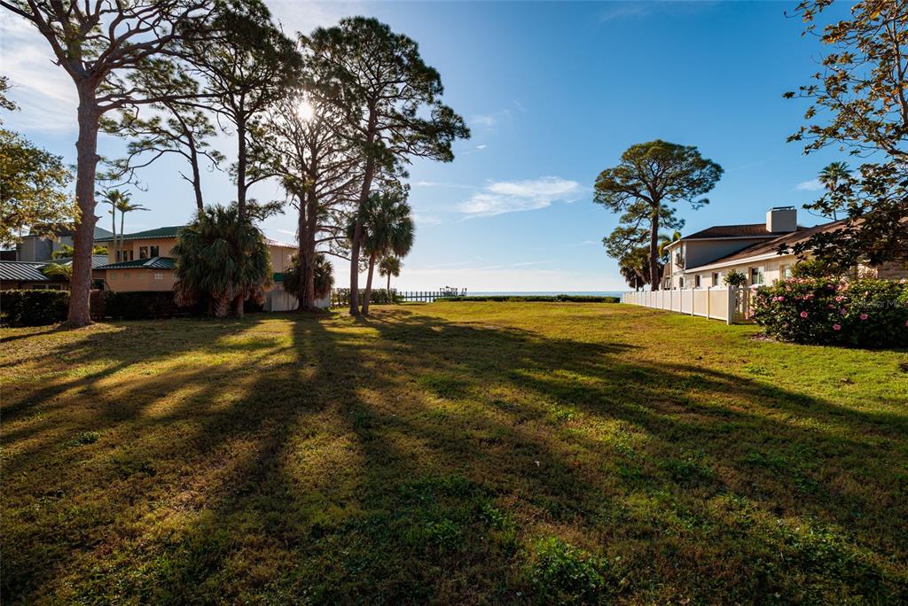 A grassy lot sits between two residential buildings with tall trees and a distant ocean view — FRIENDLY WAY S, ST PETERSBURG, FL
