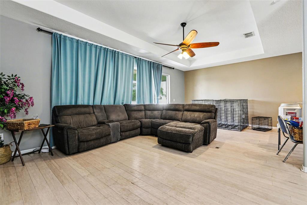 An open-concept living and dining area features light wood flooring and a tray ceiling — 2130 ROANOKE SPRINGS DRIVE, RUSKIN, FL