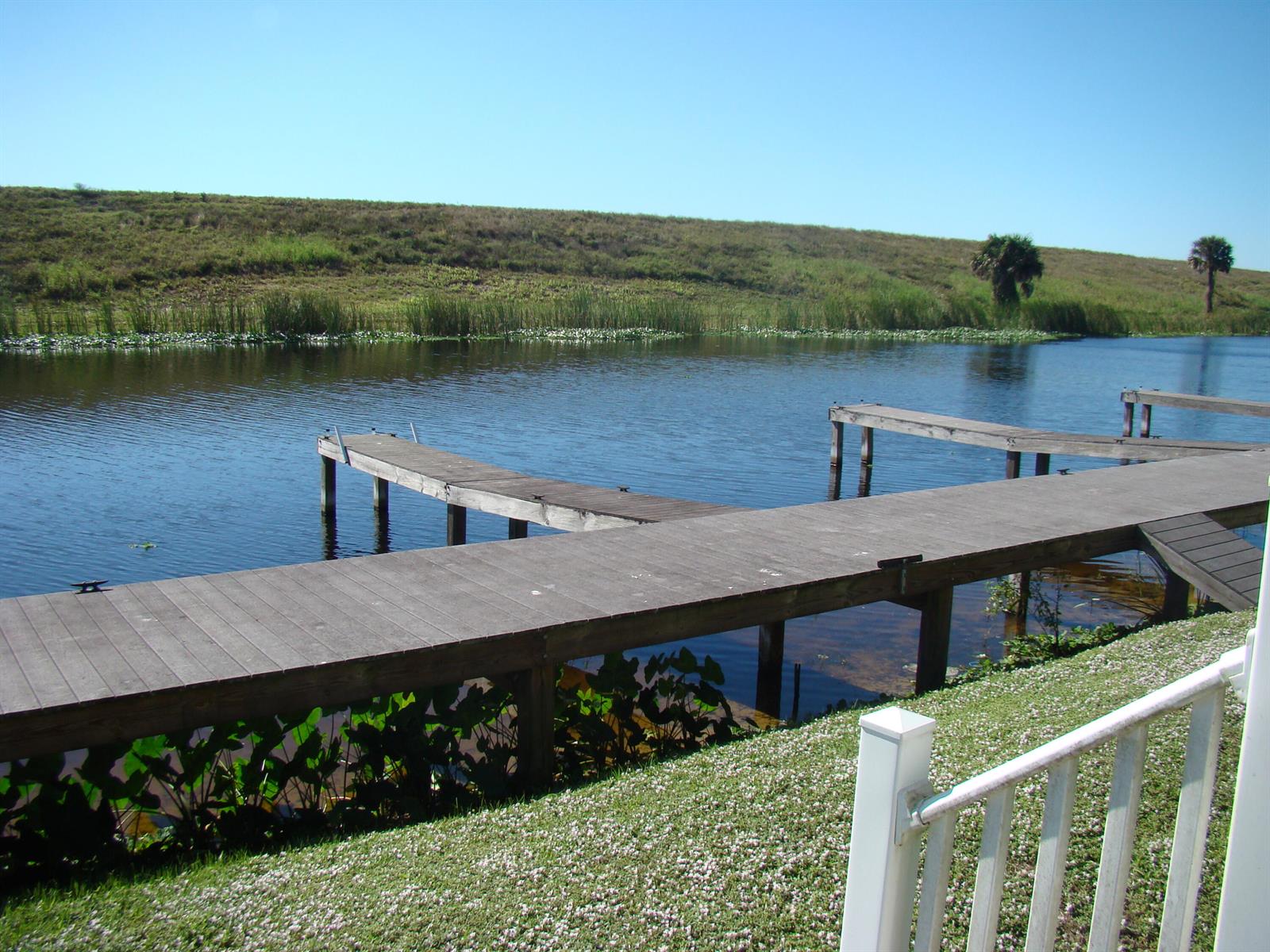 A wooden dock extends into a calm pond with a grassy hill in the background — 4334 Us Highway 441 Highway SE # 23, Okeechobee FL 34974, OKEECHOBEE, FL