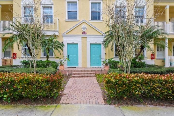 The exterior of a yellow townhouse building features two turquoise front doors and landscaping — 118 Seagrape Dr # 105, Jupiter FL 33458, JUPITER, FL