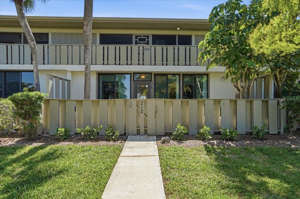 A two-story apartment building exterior features a ground-level patio with a fenced gate — 6500 FLOTILLA DRIVE UNIT 212, HOLMES BEACH, FL