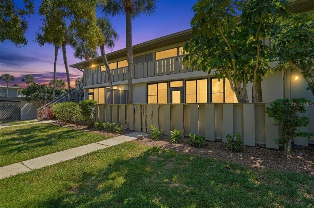 A two-story apartment building exterior features a ground-level patio with a wooden privacy fence — 6500 FLOTILLA DRIVE UNIT 212, HOLMES BEACH, FL