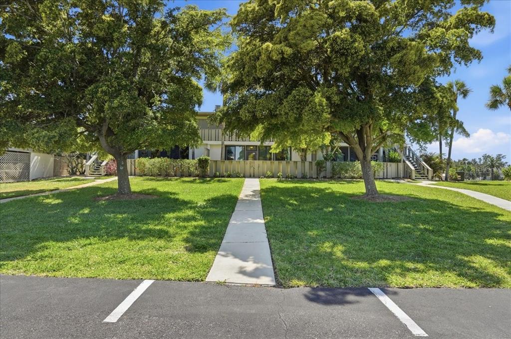 A sidewalk leads through a grassy lawn to a two-story apartment building with trees — 6500 FLOTILLA DRIVE UNIT 212, HOLMES BEACH, FL
