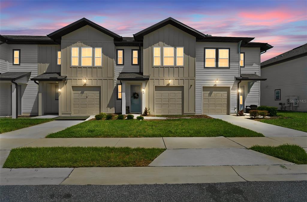 A row of three modern townhomes with light-colored siding, gabled roofs, and attached garages — 832 LONGBOAT DRIVE, DAVENPORT, FL