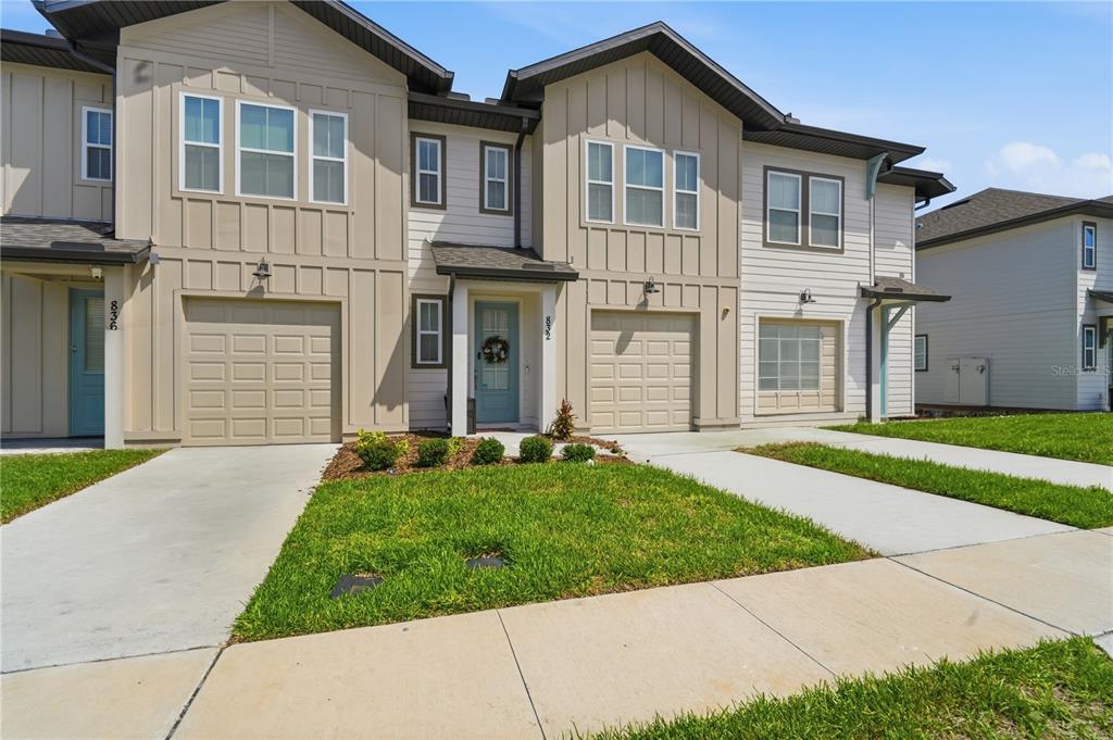 A two-story townhouse exterior with tan siding, a garage, and a small front lawn — 832 LONGBOAT DRIVE, DAVENPORT, FL