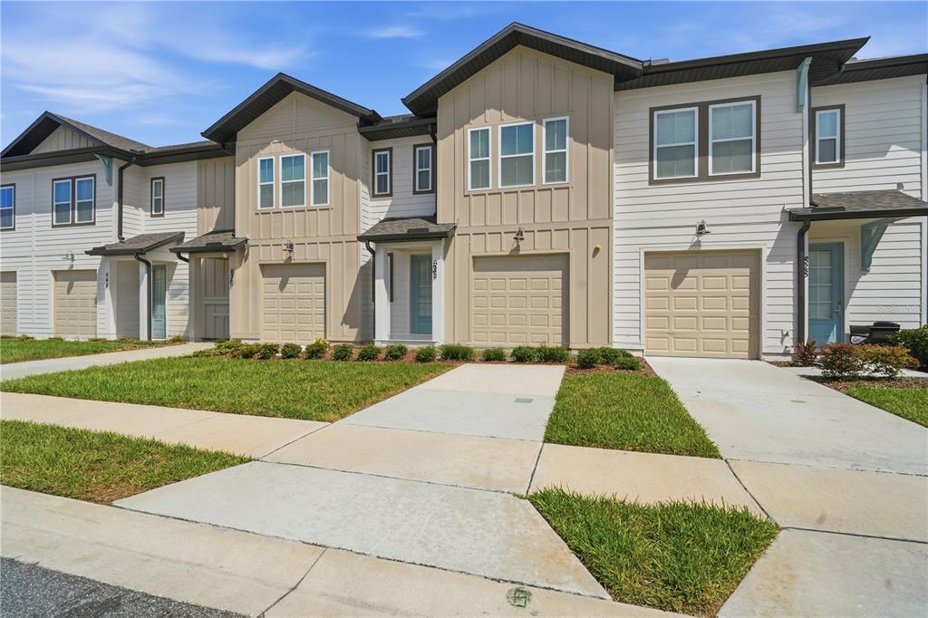 A row of modern two-story townhomes with tan and white siding, garages, and concrete driveways — 832 LONGBOAT DRIVE, DAVENPORT, FL