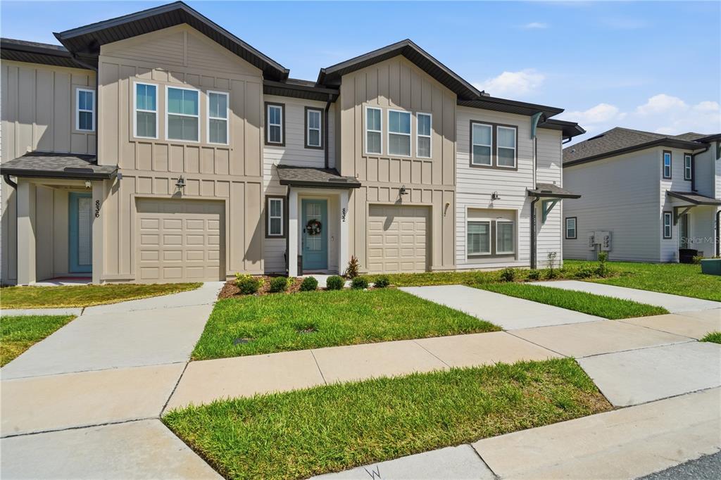 A two-story townhouse exterior features tan and white siding with two attached garages — 832 LONGBOAT DRIVE, DAVENPORT, FL