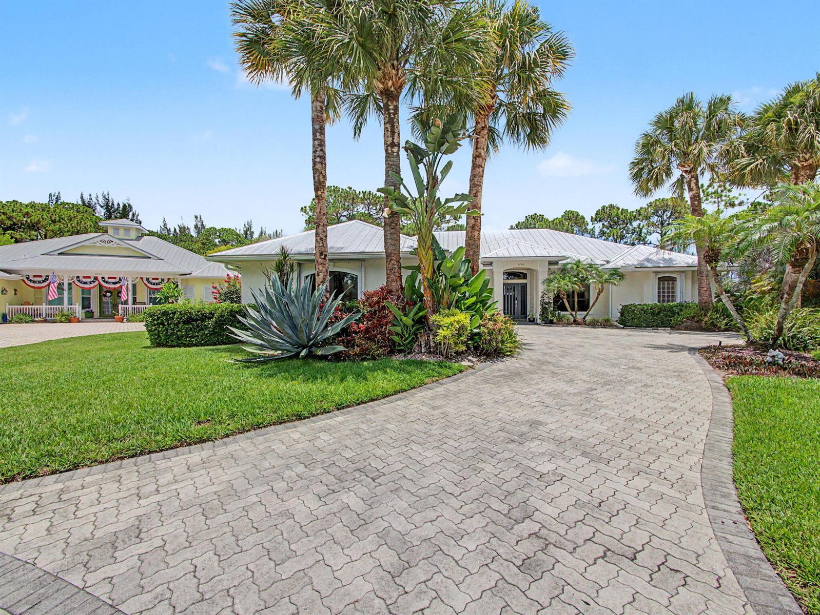 A paved driveway leads to a light-colored house with palm trees and landscaping — 8780 SW Fishermans Wharf Drive, Stuart FL 34997, STUART, FL